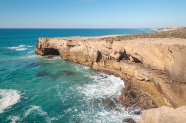 Odemira, Portekiz 'deki Vila Nova de Milfontes yakınlarındaki Atlantik kıyısında, öğleden sonra güneşinde dalgalanan dalgalarla nefes kesici uçurumlar. Rota Vicentina 'nın izinden. Balıkçı yolu. Açık mavi gökyüzü.