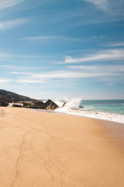 Atlantik Okyanusu 'nun dalgaları güneşli bir günde Portekiz' in batısındaki Porto Covo yakınlarındaki Praia da Ilha do Pessegueiro kumsalında bir kayaya çarpıyor. Rota Vicentina..