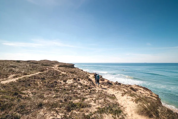 Passionate adventurers walk the rugged, dry coastline with cliffs around the Atlantic Ocean on a trail called the Fisherman Trail in Portugal.