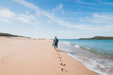 Tutkulu bir sırt çantası ve elinde botlarıyla Portekiz 'in Porto Covo yakınlarındaki Atlantik Okyanusu kıyısındaki Praia da Ilha do Pessegueiro plajı boyunca yürüyor. Rota Vicentina 'nın izinden..