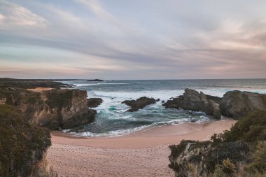 Praia dos Buizinhos 'un kumlu plajının güzelliği Porto Covo' da kayalıklarla gün batımında Portekiz 'in batısında, Rota Vicentina yürüyüşünün başlangıcında.