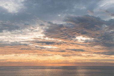 Güneşin son ışınları gökyüzünde uçan bulutları aydınlatır ve denizden yansıyan yansıma çevredeki uçurumları aydınlatır. Renklerin ahengi. Rüya gibi. Portekiz 'in Algarve bölgesinde gün batımı.