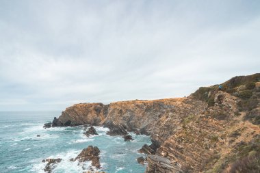 Yürüyüşçü, Portekiz 'in batısındaki Algarve' nin ünlü turistik bölgesindeki Ohexe kasabası yakınlarındaki Atlantik Okyanusu 'nun engebeli kaya ve uçurum kıyısında yer almaktadır. Gün batımı.