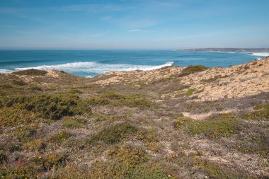 Portekiz 'in batısındaki Odemira bölgesinde güneşli bir günde Atlantik kıyısında dağlık ve dengesiz kayalık bir manzara. Balıkçı Patikası boyunca gezinen, Rota Vicentina.