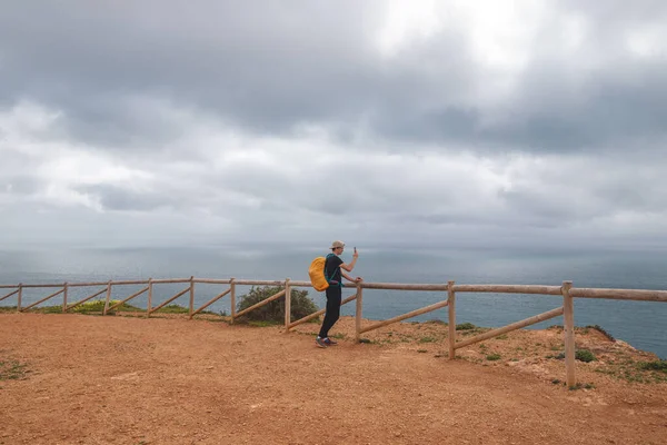 Gezgin, Portekiz 'in güneyindeki Algarve bölgesindeki Atlantik Okyanusu kıyıları ve Luz şehrine bakan Atalaia Tepesi' nin tepesindeki cep telefonuyla fotoğraf çekiyor..