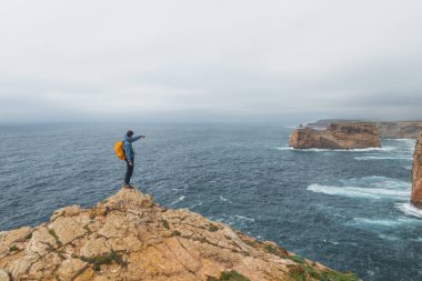 Siyah saçlı maceracı, Portekiz 'in güneybatısındaki Cabo de Sao Vicente Burnu' nun sonunda duruyor. Kayalık kayalıkları seyrediyorum. Balıkçı Yolu 'nun Gezgini.