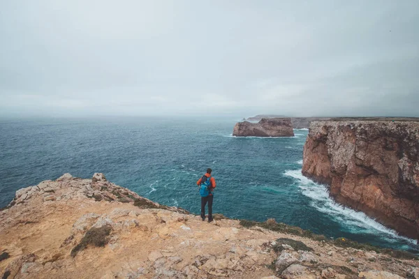 stock image Black-haired adventurer stands at the end of Cape Cabo de Sao Vicente in the southwest of Portugal in the Algarve region. Man is enjoying his freedom. Wandering of Fisherman Trail.