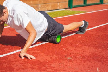 Atletik oval vücut yapısı olan kahverengi saçlı çocuk daha iyi iyileşmek için kaslarına köpük silindirle masaj yapıyor. Egzersiz sonrası.