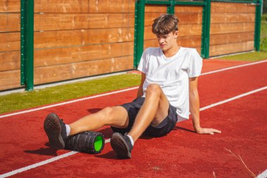 Atletik oval vücut yapısı olan kahverengi saçlı çocuk daha iyi iyileşmek için kaslarına köpük silindirle masaj yapıyor. Egzersiz sonrası.