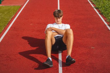 Atletik oval vücut yapısı olan kahverengi saçlı çocuk daha iyi iyileşmek için kaslarına köpük silindirle masaj yapıyor. Egzersiz sonrası.