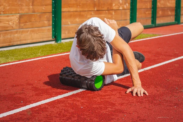 Atletik oval vücut yapısı olan kahverengi saçlı çocuk daha iyi iyileşmek için kaslarına köpük silindirle masaj yapıyor. Egzersiz sonrası.