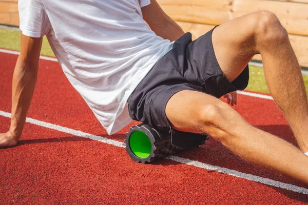 Atletik oval vücut yapısı olan kahverengi saçlı çocuk daha iyi iyileşmek için kaslarına köpük silindirle masaj yapıyor. Egzersiz sonrası.