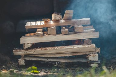 Mükemmel bir alev yaratmak için piramit şekillerinde kağıt ve küçük odun parçaları kullanarak ateş yakıyor..