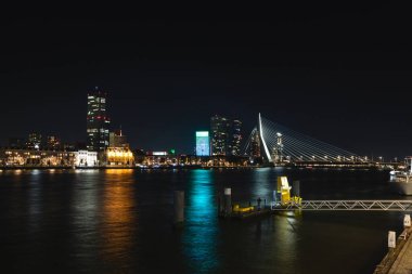 Hollanda, Rotterdam 'da gece geç saatlerde bir sürü aydınlık gökdelen bulunan kanalın ve zıt aydınlık bankanın manzarası.