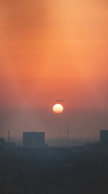 Amsterdam üzerinden geçen uçak gün batımında güneş diskine dalıyor. Modern zamanlarda seyahat etmek. Şehir sise gömüldü ve turuncu bir gökyüzü.