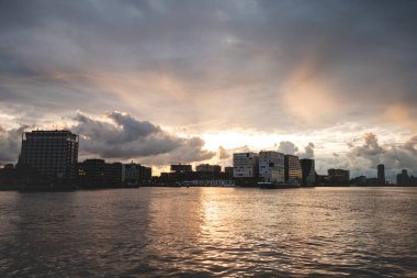 Gün batımı boyunca fırtına bulutları Amsterdam şehrinde dolaşır ve dramatik bir atmosfer yaratır. Hollanda yaşam tarzı ve modern şehir manzarası.