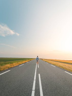 Kahverengi saçlı, kareli gömlekli bir adam gün batımında Hollanda, Almere 'in eteklerinde yol boyunca yürür. Moda yaşam tarzı.