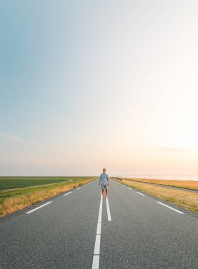 Kahverengi saçlı, kareli gömlekli bir adam gün batımında Hollanda, Almere 'in eteklerinde yol boyunca yürür. Moda yaşam tarzı.