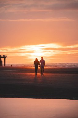 Batı Belçika 'nın Oostende sahillerinde gün batımında genç bir çiftin romantik yürüyüşü. Sevgi ve bağlılık. Su havuzundaki yansıma..