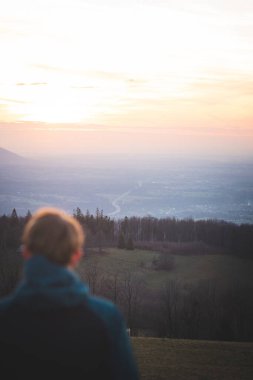25-29 yaşlarındaki sarışın adam Beskydy dağlarındaki Trinec yakınlarında Loucka dağının tepesinde gün batımını izliyor..