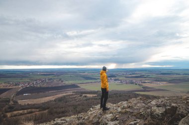 Sarı ceketli gezgin Rip Dağı 'nın tepesinde duruyor ve Prag şehrini işaret ediyor. Çek ülkesini keşfetmek.