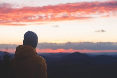 Çek Cumhuriyeti üzerinden gün batımını ve turuncu-kırmızı renkli bulutları izleyen bir gezginin arka görüntüsü. Yürüyüş yaşam tarzı.