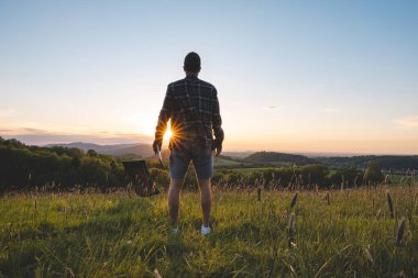 Genç adam gün batımında bir çayıra bir sandalye yerleştirir ve vadiyi ve ufukta batan güneşi görmeye hazırlanır. Beskydy Dağları, Çek Cumhuriyeti.