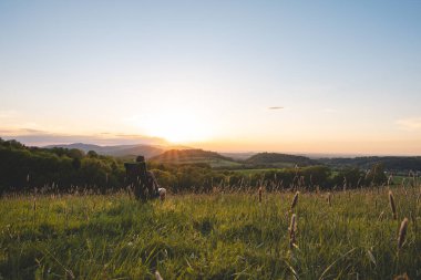 Ekose gömlekli genç adam seyyar bir hafif koltukta oturur, vadinin manzarasının ve ufukta batan güneşin tadını çıkarır. Beskydy Dağları, Çek Cumhuriyeti.