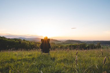 Ekose gömlekli genç adam seyyar bir hafif koltukta oturur, vadinin manzarasının ve ufukta batan güneşin tadını çıkarır. Beskydy Dağları, Çek Cumhuriyeti.