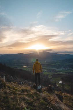 Adventurous man standing on a tree stump and observing the sunrise in the Beskid Mountains in the Czech Republic. The breathtaking scenery and the rising sun create picturesque moment. clipart