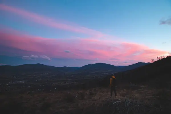 stock image Adventurer stands on a stump and watches the remnants of the sunlight that causes the clouds above him to turn colour. Pinkish-red clouds in the early evening in the east of the Czech Republic.