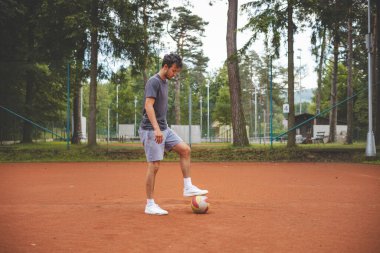 20 'li yaşlardaki futbolcu kil sahada bir balonla oynuyor. Amatör spor. Bireysel futbol eğitimi. - Futbol. Tekme, vuruş, pas ve top sürme.