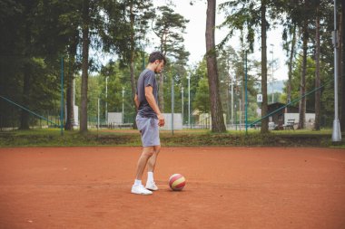 20 'li yaşlardaki futbolcu kil sahada bir balonla oynuyor. Amatör spor. Bireysel futbol eğitimi. - Futbol. Tekme, vuruş, pas ve top sürme.