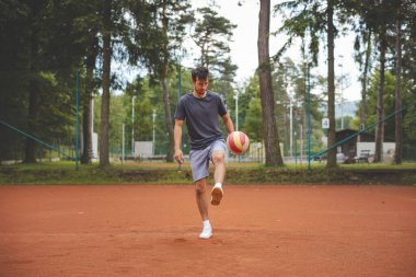 20 'li yaşlardaki futbolcu kil sahada bir balonla oynuyor. Amatör spor. Bireysel futbol eğitimi. - Futbol. Tekme, vuruş, pas ve top sürme.