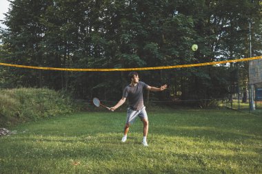 Siyah saçlı badminton oyuncusu vuruşlarını çimen kortunda yapıyor. Bireysel teknik eğitimi. Sporun amatör konsepti. Oyunun neşesi.