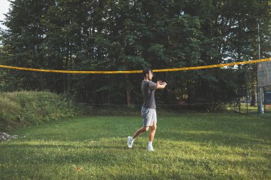 Siyah saçlı badminton oyuncusu vuruşlarını çimen kortunda yapıyor. Bireysel teknik eğitimi. Sporun amatör konsepti. Oyunun neşesi.
