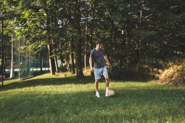 Siyah saçlı atlet çimlerde dostça bir futbol maçı oynar. Amatör spor. Topla oynayan bir adam. Salya sürme alıştırması. Spor yaşam tarzı.