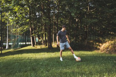 Siyah saçlı atlet çimlerde dostça bir futbol maçı oynar. Amatör spor. Topla oynayan bir adam. Salya sürme alıştırması. Spor yaşam tarzı.