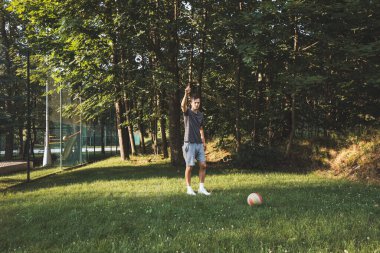 Siyah saçlı atlet çimlerde dostça bir futbol maçı oynar. Amatör spor. Topla oynayan bir adam. Salya sürme alıştırması. Spor yaşam tarzı.