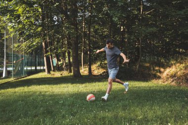 Siyah saçlı atlet çimlerde dostça bir futbol maçı oynar. Amatör spor. Topla oynayan bir adam. Salya sürme alıştırması. Spor yaşam tarzı.