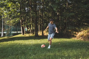 Siyah saçlı atlet çimlerde dostça bir futbol maçı oynar. Amatör spor. Topla oynayan bir adam. Salya sürme alıştırması. Spor yaşam tarzı.