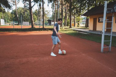 Siyah saçlı sporcu balonla kil sahada oynuyor. Amatör spor. Bireysel futbol eğitimi. - Futbol. Tekme, vuruş, pas ve top sürme.