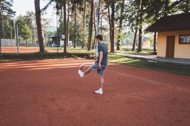 Siyah saçlı sporcu balonla kil sahada oynuyor. Amatör spor. Bireysel futbol eğitimi. - Futbol. Tekme, vuruş, pas ve top sürme.