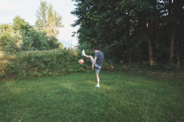 Siyah saçlı atlet çimlerde dostça bir futbol maçı oynar. Amatör spor. Topla oynayan bir adam. Salya sürme alıştırması. Spor yaşam tarzı.