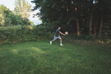 Siyah saçlı atlet çimlerde dostça bir futbol maçı oynar. Amatör spor. Topla oynayan bir adam. Salya sürme alıştırması. Spor yaşam tarzı.