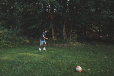 Siyah saçlı atlet çimlerde dostça bir futbol maçı oynar. Amatör spor. Topla oynayan bir adam. Salya sürme alıştırması. Spor yaşam tarzı.
