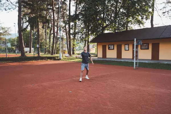 Yüzünde gülümseme olan siyah saçlı bir sporcu kil sahada badminton oynar. Amatör spora olan tutkum. Yeni hareket becerileri öğreniliyor.