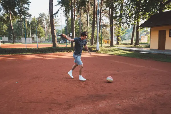 Siyah saçlı sporcu balonla kil sahada oynuyor. Amatör spor. Bireysel futbol eğitimi. - Futbol. Tekme, vuruş, pas ve top sürme.