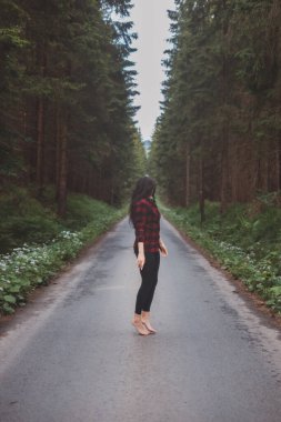 20-25 yaşlarındaki esmer, siyah taytlı ve ekose gömlekli bir kadın orman ortamında dans ediyor. Hareket ve temiz havanın keyfi. Orman Perisi.