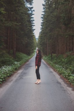 20-25 yaşlarındaki esmer, siyah taytlı ve ekose gömlekli bir kadın orman ortamında dans ediyor. Hareket ve temiz havanın keyfi. Orman Perisi.